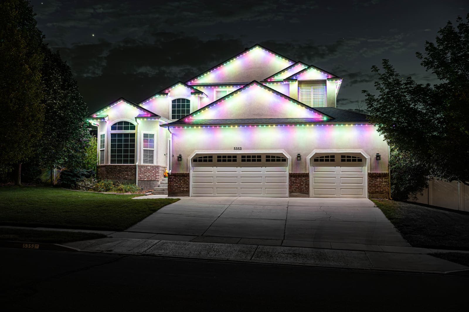 A two-story Houston home at dusk with its roofline lit in festive holiday colors.